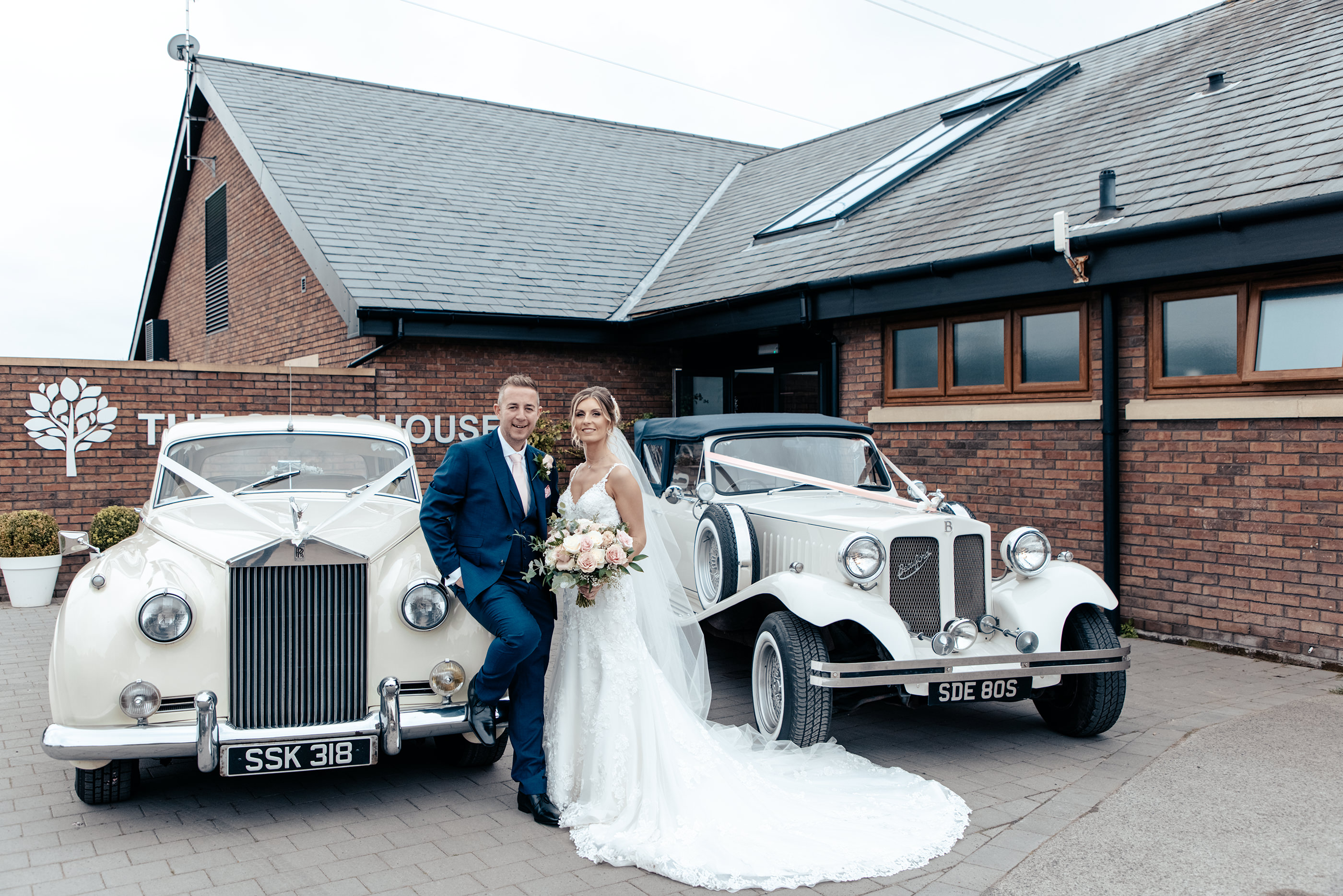 The bride and groom with the wedding cars 