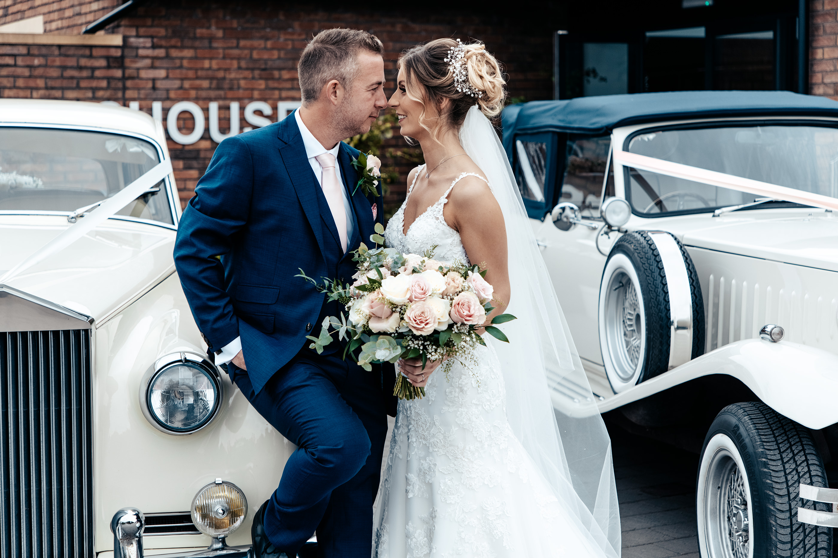 The bride and groom with the wedding cars 