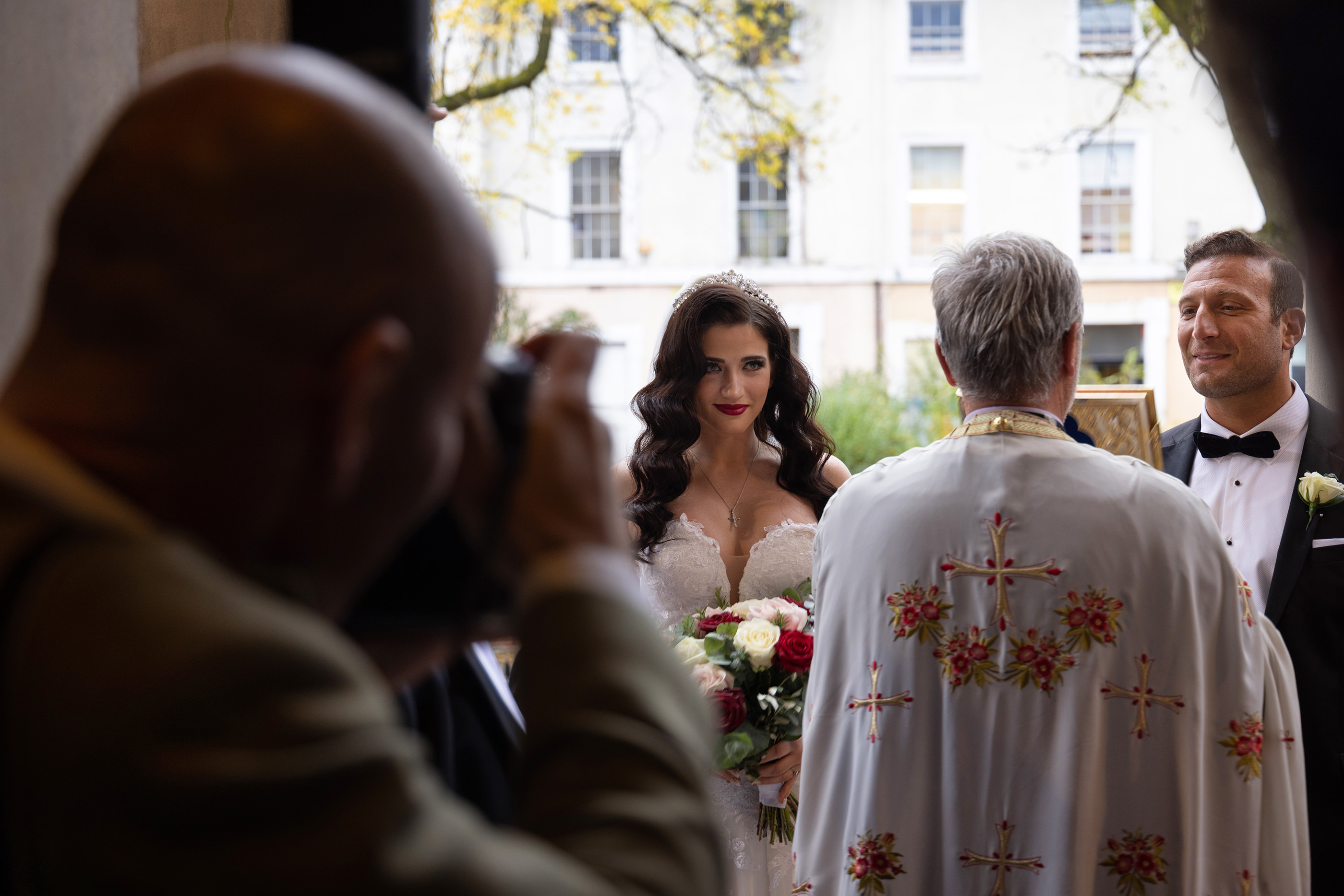 Madalina and Stelios  are greeted by the Greek priest