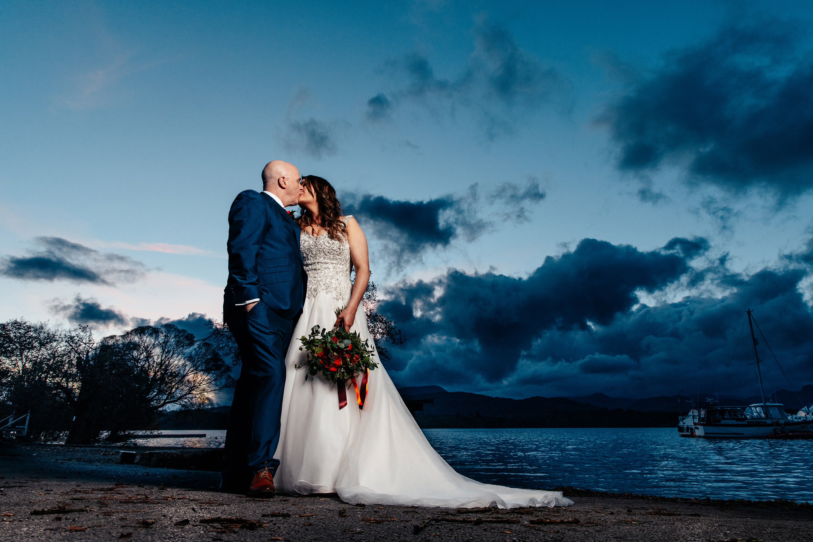  the bride and groom have a kiss on the edge of lake windermere