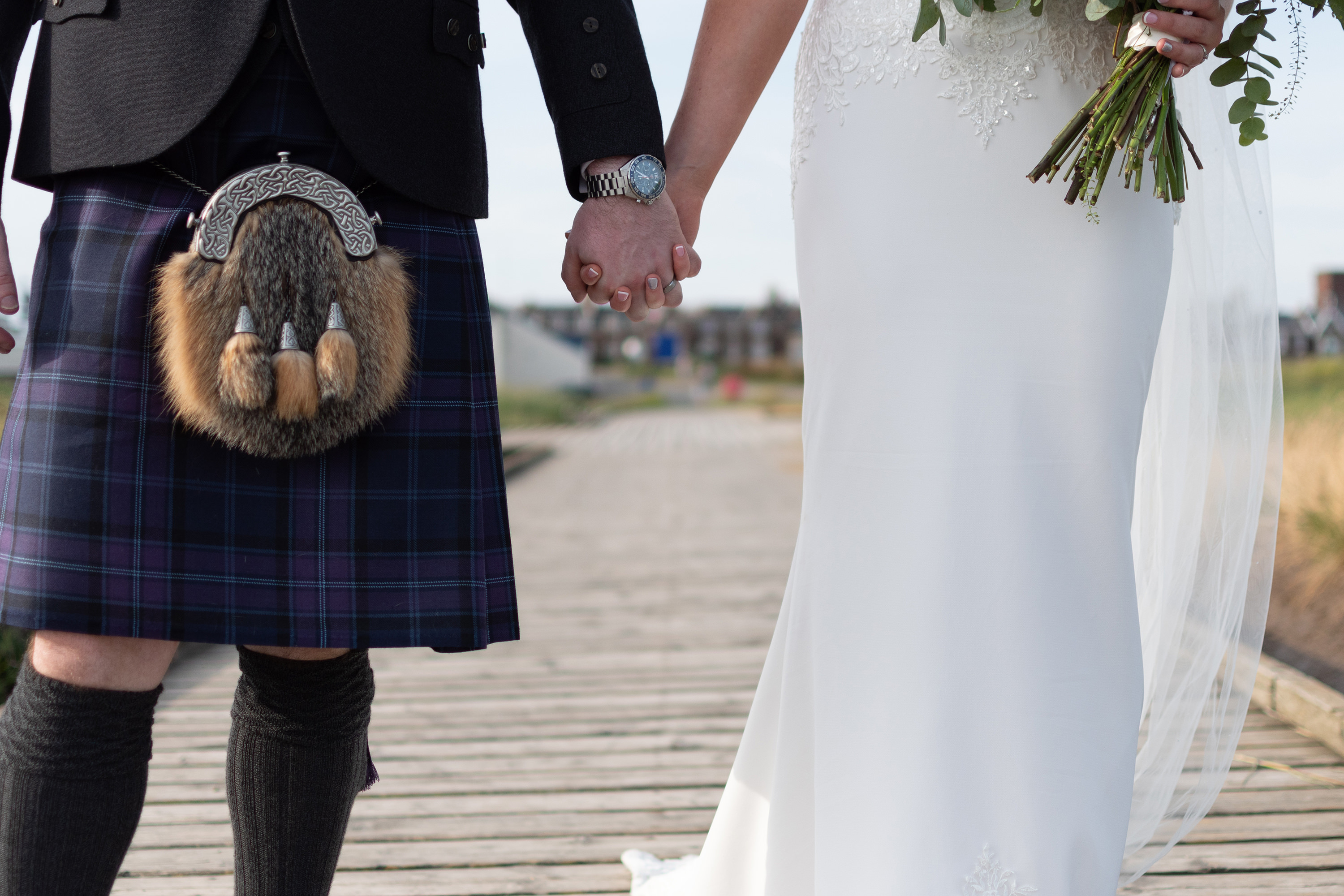 The bride and groom holding hands as they walk down the jetty in Lytham 