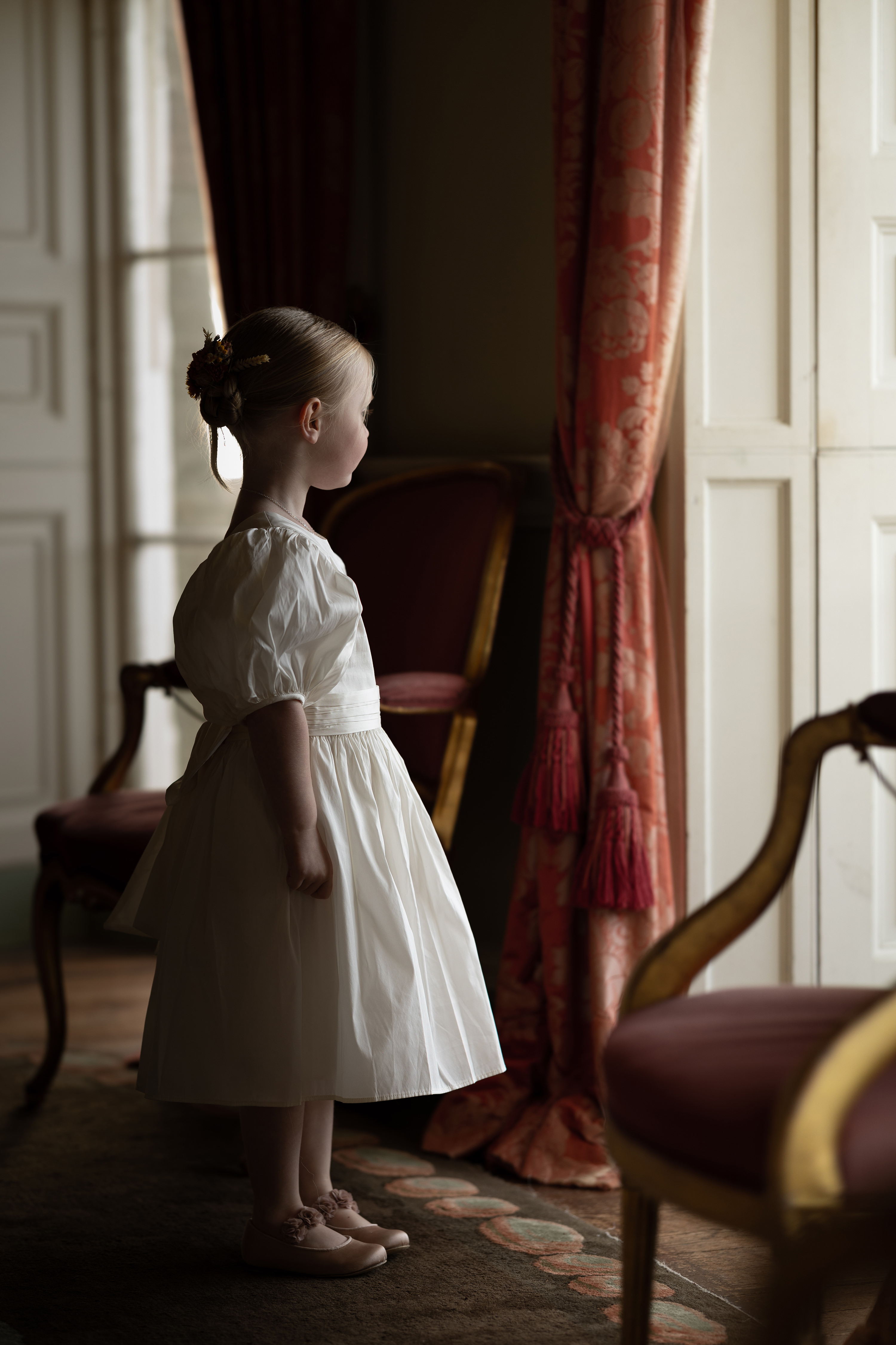 A little girl stands in front of the window in the drawing room 