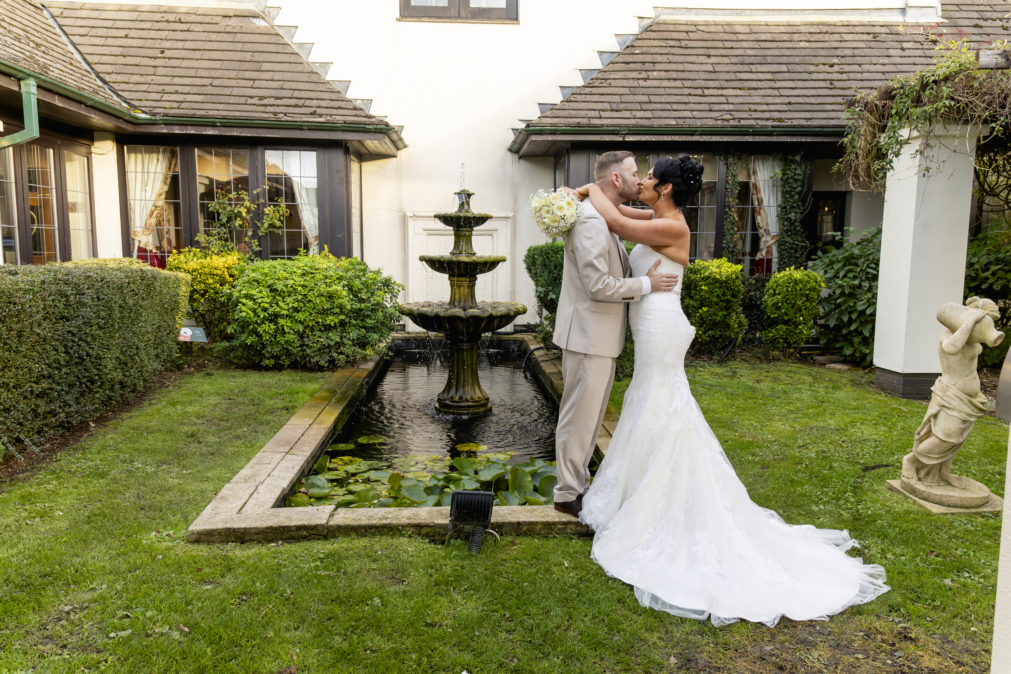 The bride and groom pose for a photo by the fountain 